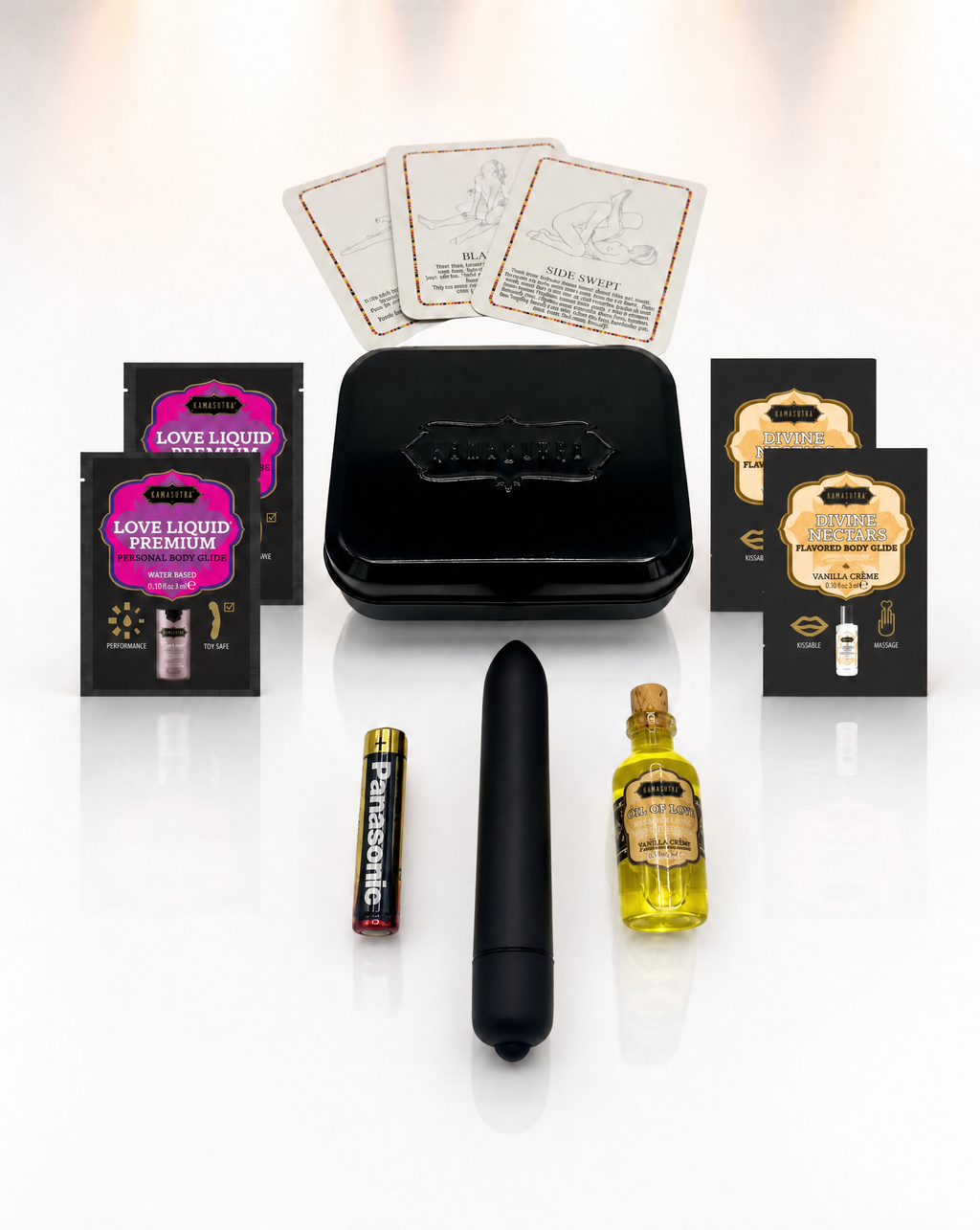 A photo showing the contents of the Kama Sutra weekender vibe kit in Vanilla Creme. There is 3 position cards, 2 Love Liqud packets, two Divine Nectar Vanilla Creme packets, a black bullet vibe with battery and a mini glass Oil of Love outside a black tin.