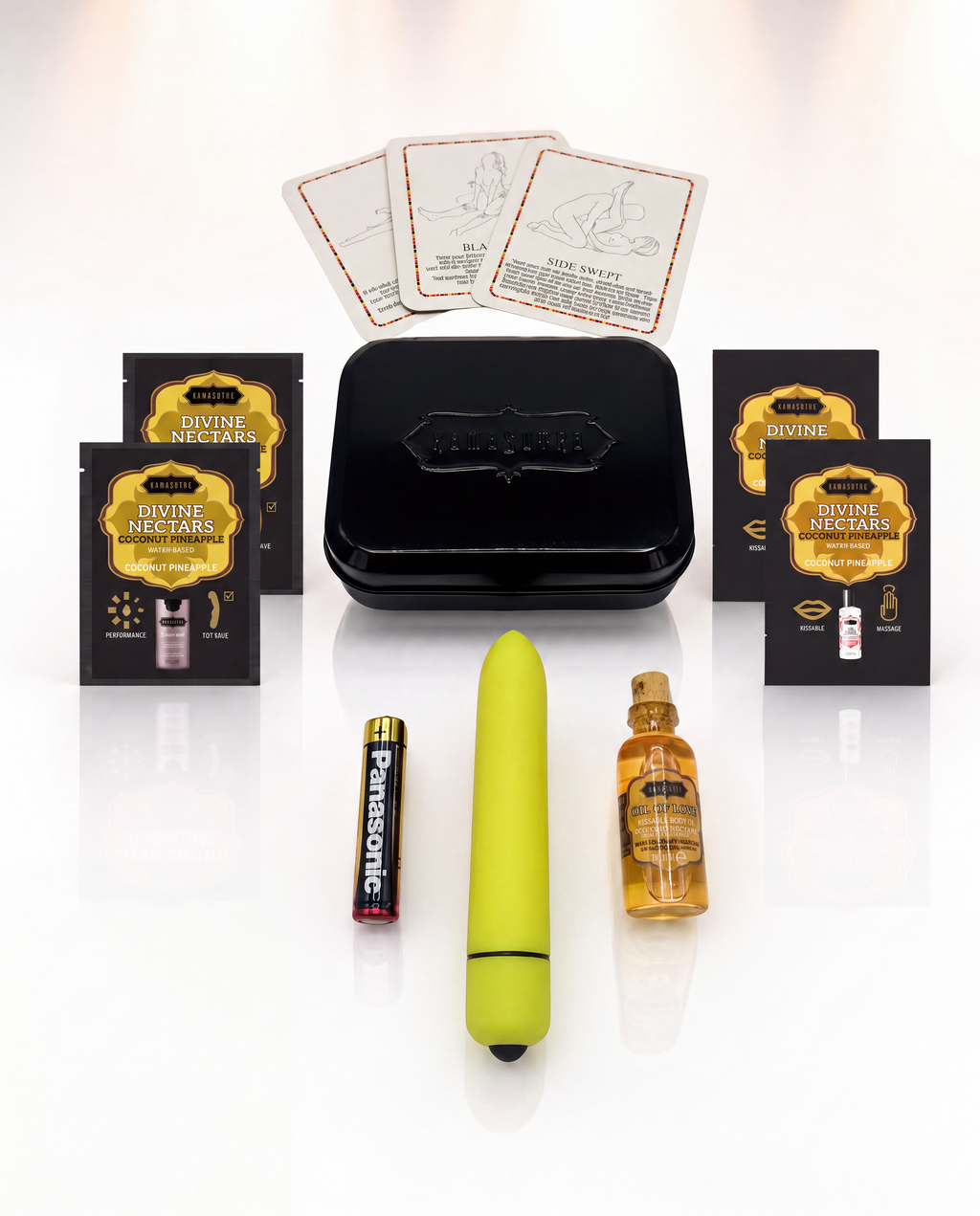 A photo showing the contents of the Kama Sutra weekender vibe kit in Coconut Pineapple. There is 3 position cards, 2 Love Liqud packets, two Divine Nectar Coconut Pineapple packets, a yellow bullet vibe with battery and a mini glass Oil of Love outside a black tin.