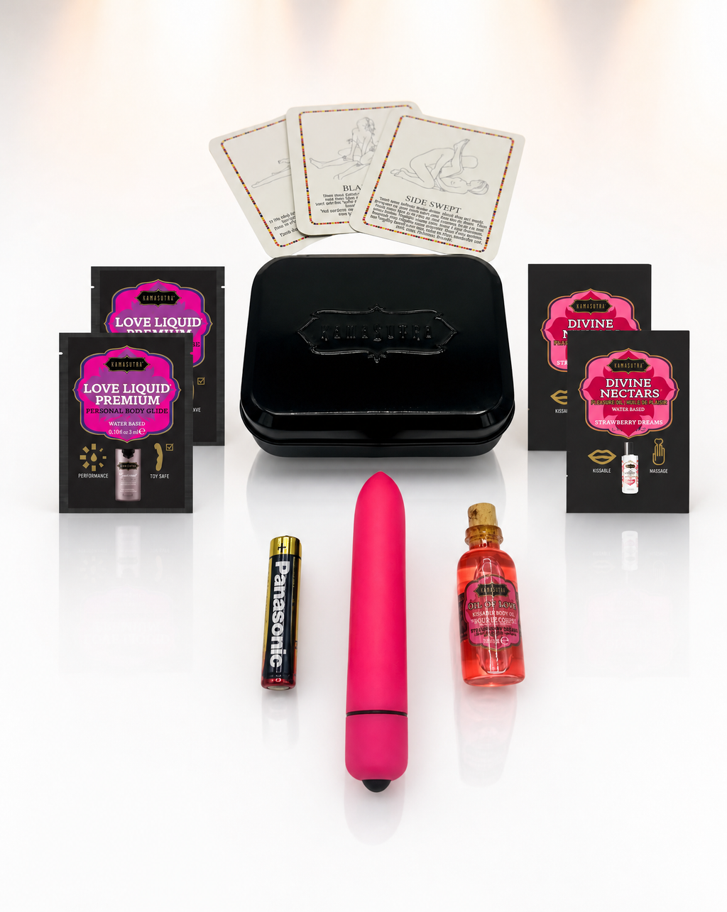 a photo showing the contents of the kama sutra weekender vibe kit in Strawberry Dream. There is 3 position cards, 2 Love Liqud packets, two divine nectar strawberry packets, a pink bullet vibe with battery and a mini glass oil of love outside a black tin.