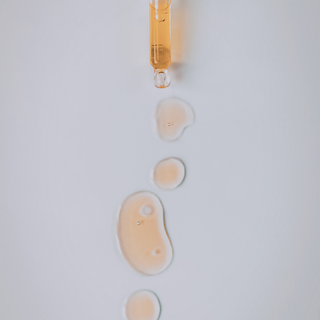 Amber-colored oil droplet being released from a pipette onto a white surface.