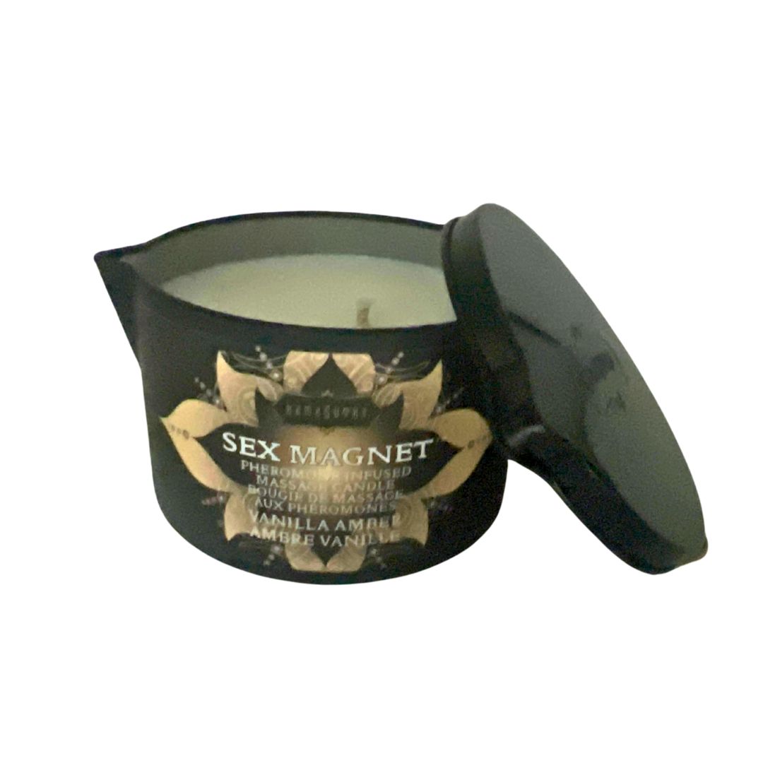 A black container with a lid labeled SEX MAGNET™ Pheromone Massage Candle, with a white candle inside. The container has a decorative design with gold accents and text indicating the scent as Vanilla Amber. shown in 6 oz size