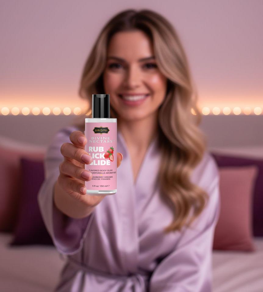 Woman in a robe holding a bottle of Kama Sutra Divine Nectars in  STRAWBERRY Dreams FLAVOR  product in a bedroom setting.