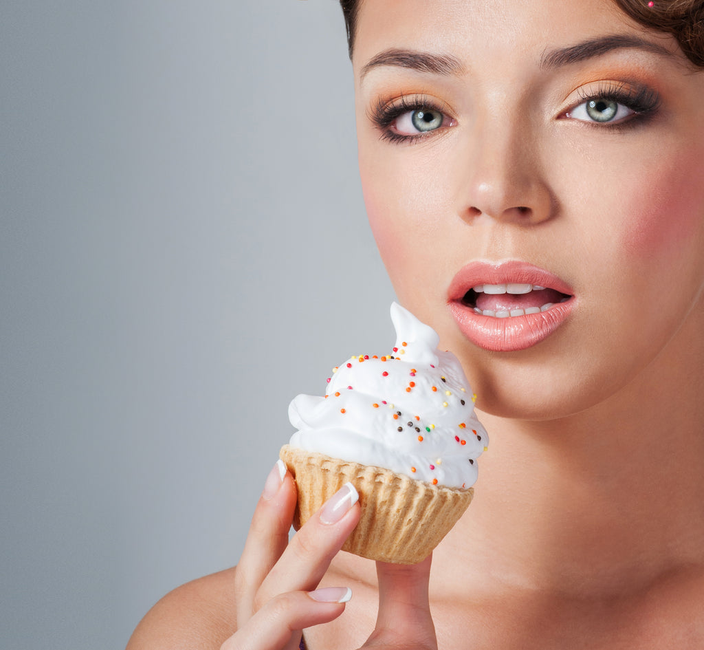 Woman holding a cupcake with white frosting and colorful sprinkles against a gray background