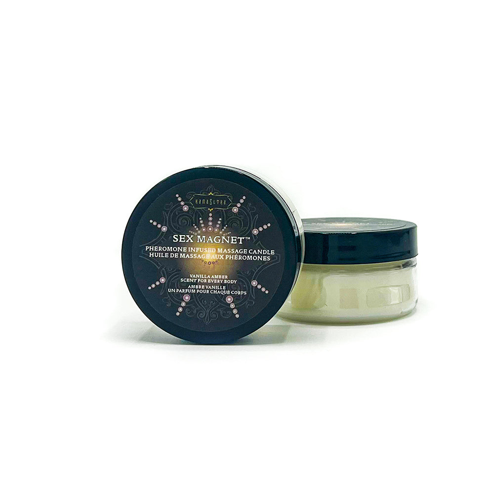 A clear container with a black lid labeled SEX MAGNET™ Pheromone Massage Candle, with a white candle inside. The container has a decorative design with gold accents and text indicating the scent as Vanilla Amber. shown in 1.7 oz size